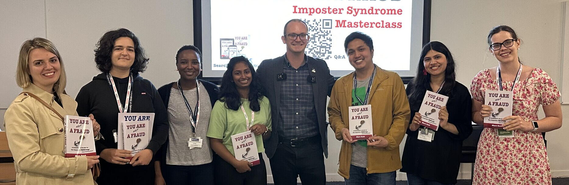 Imposter Syndrome Masterclass learning outcomes. Marc Reid, workshop host, surrounded by workshop cohort members holding their copies of the book, You Are (Not) a Fraud.